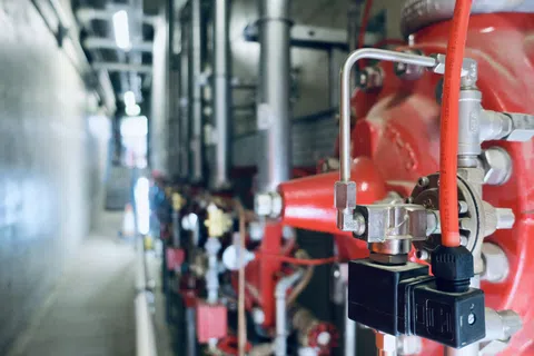 Close-up of industrial red fire safety pipe system with valves and pressure gauges in a mechanical room.