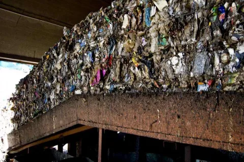 Large compressed bale of mixed recyclables stacked under a concrete structure in a recycling facility.