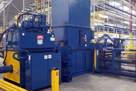 Large blue and yellow industrial machine inside spacious warehouse with metal shelving and concrete floor.