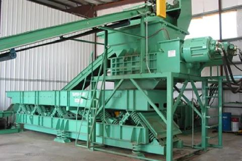 Large green industrial machine inside warehouse with conveyor belts and metal framework for processing materials.