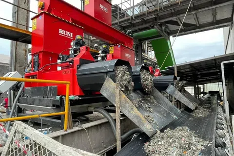 Red RUNI machines sorting and processing waste materials onto conveyor belts in industrial recycling facility