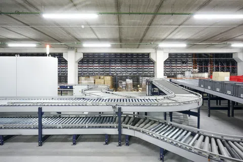 Curved metal roller conveyor system in a spacious warehouse with shelves and boxes in the background.