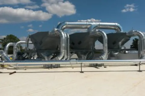 Industrial HVAC system with large metallic ductwork and ventilation units on a rooftop under a partly cloudy sky