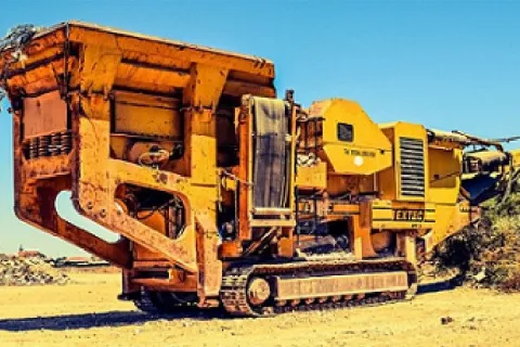 Large yellow industrial wood chipper machine operating outdoors on dry ground under clear sky