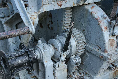 Close-up of rusted metal gears and levers painted gray on old industrial machinery.