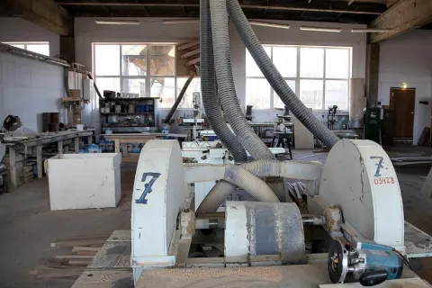 Industrial woodworking machine with large hoses in a spacious workshop full of tools and equipment.