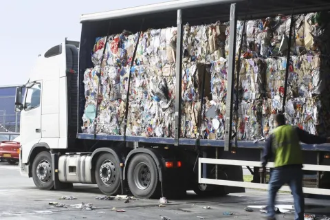 Large truck loaded with compressed recyclable cardboard and paper bales at a recycling facility with worker nearby