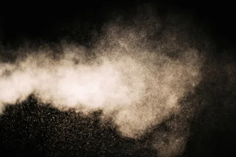 Fine powder particles suspended in air forming a cloud against a dark background.