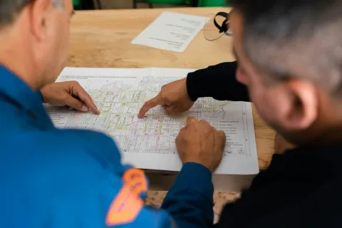 Two men reviewing and pointing at architectural plans on a wooden table during a meeting.