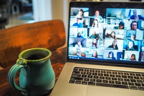 Laptop showing a video conference with many participants and a green ceramic coffee mug on a wooden table