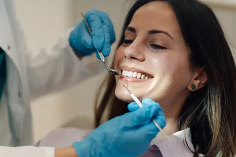 Patient smiling while dentist wearing blue gloves examines teeth with dental tools during checkup