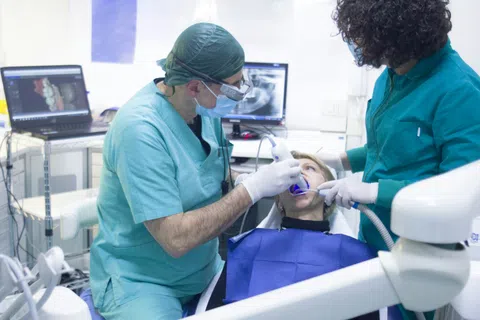 Dentist and assistant treating female patient in dental clinic with digital X-ray screens in background