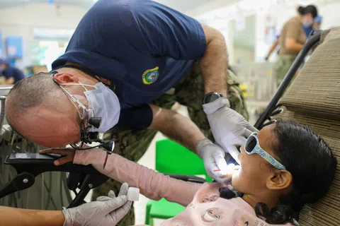 Dentist wearing mask and gloves examining young girl's teeth in a dental clinic with focused care.