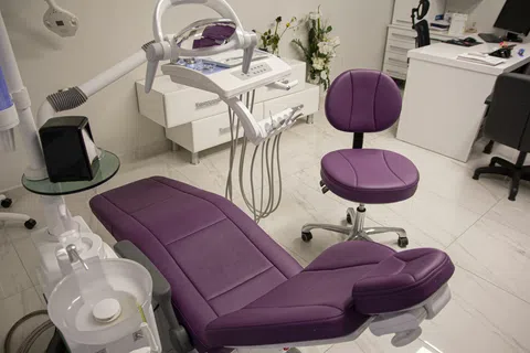 Modern dental clinic interior with purple dental chair, equipment, and workstations in a clean, bright room