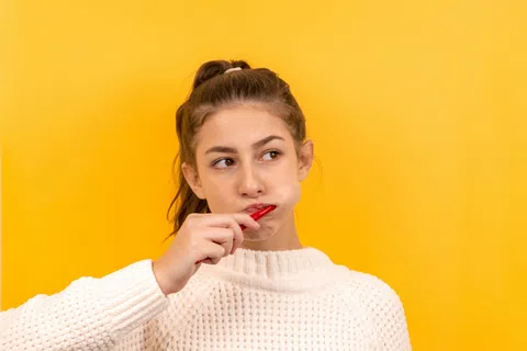 Young woman brushing her teeth with a red toothbrush against a bright yellow background