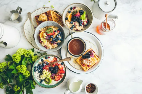 Top view of healthy breakfast bowls with fresh fruit, waffles, honey, and coffee on a marble table.