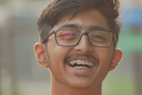 Smiling young man with braces wearing glasses and a red shirt outdoors in soft natural light