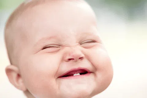 Close-up of smiling baby with eyes closed showing two front teeth and joyful expression