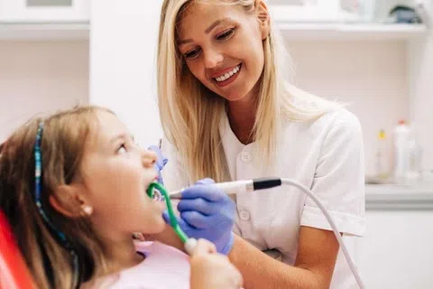Smiling female dentist treating young girl patient using dental tools in modern clinic