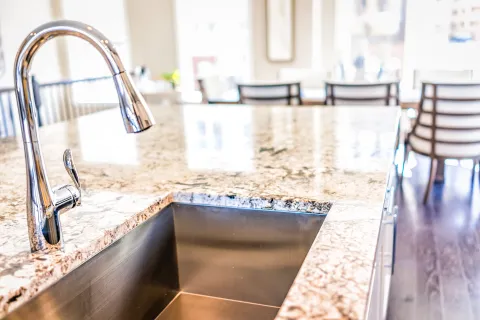 Close-up of a sleek kitchen sink integrated into a polished granite countertop with modern furnishings.