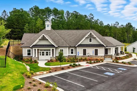 Modern single-story community building with stone accents, landscaped grounds, and empty parking lot surrounded by trees.
