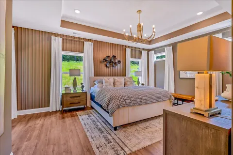 Modern bedroom with beige bed, patterned bedding, wooden floors, nightstands, and gold chandelier light fixture.