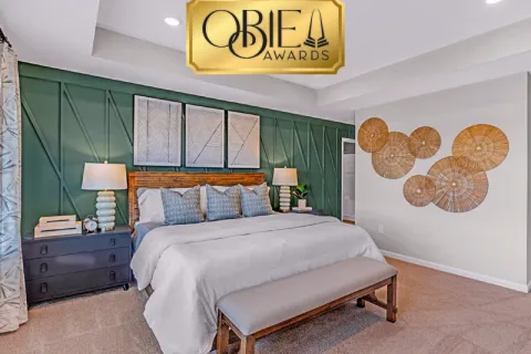 Cozy modern bedroom with green accent wall, white bedding, wooden bench, and decorative woven wall art.