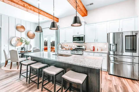 Bright modern kitchen with large island, granite countertop, stainless steel appliances, and wooden beams