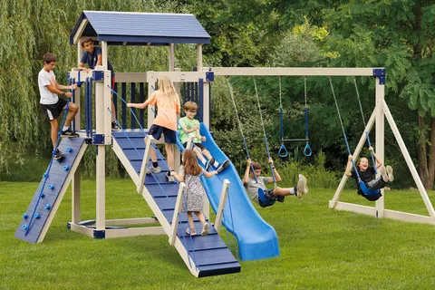 Children playing on a wooden playground set with slide, swings, and climbing wall in a green park.