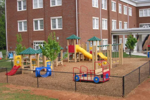 Children's playground with slides, climbing structures, and swings next to a large brick building.