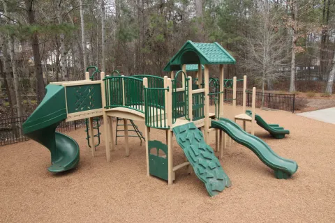 a playground with green slide and trees