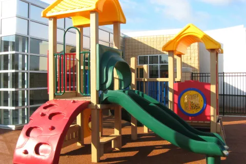 Colorful playground structure with slides, climbing wall, and play panels on soft safety surface outdoors.