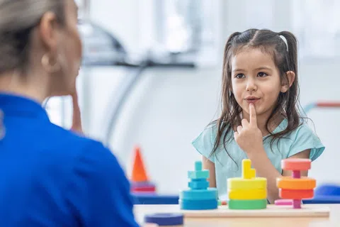 Young girl engaging with a therapist using colorful stacking toys in a bright therapy room.