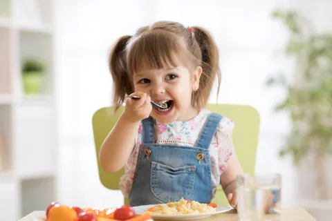 Happy young girl enjoying her meal with fruits and water at a bright kitchen table.