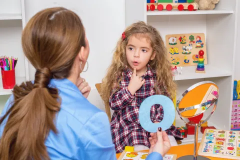 A teacher helps a young girl with letter recognition during a playful learning session.