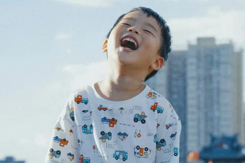 Joyful young boy laughing outdoors in a cityscape background wearing a vehicle-patterned shirt