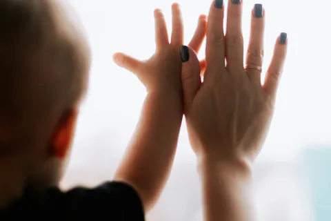 Child and adult hands touching a window, illustrating connection and growth with soft natural light.