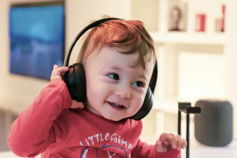 Smiling toddler wearing black headphones and a red shirt playing indoors in a bright room.