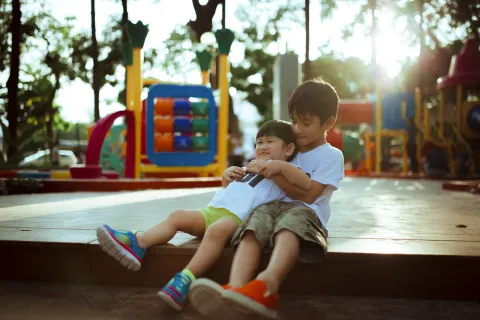 Two children playing and hugging at a colorful playground with softened sunlight in the backgrounda