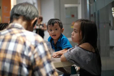 Young children interacting with an elderly man at a table in a bright indoor setting.