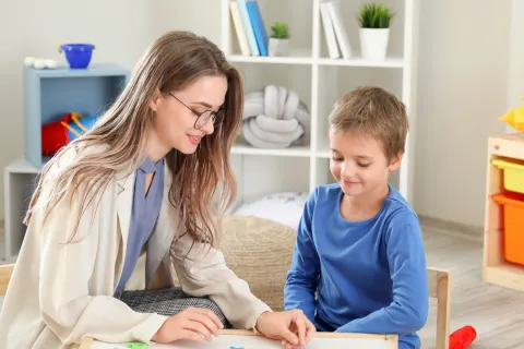 Teacher and young boy playing with colorful alphabet letters at table in classroom setting