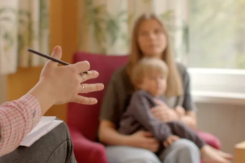 A therapist speaks with a mother holding her child during a counseling session.