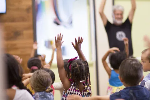 Children raising hands participating actively in a classroom with a teacher leading the session.