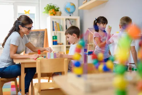 A teacher guides children in a colorful classroom, fostering creativity and collaboration through play.