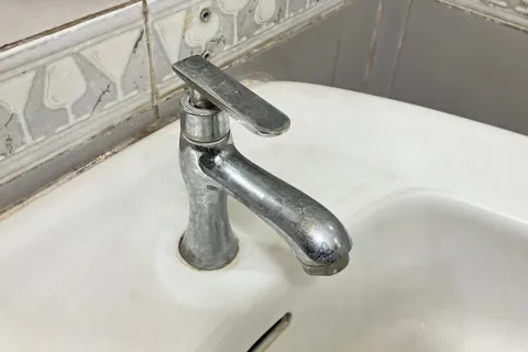 Chrome faucet mounted on a white porcelain sink with decorative patterned tile backsplash in bathroom corner.