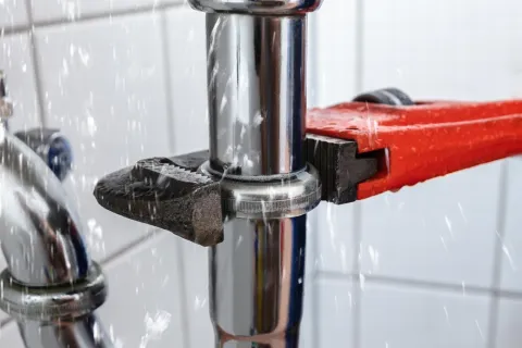 Close-up of a plumber's wrench tightening a metal pipe with water spraying from a leak.