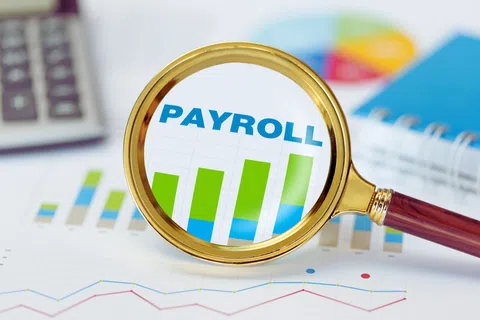 Magnifying glass highlighting the word PAYROLL and a colorful bar chart on financial documents.