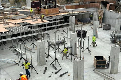 Construction workers in safety vests on concrete building site with steel supports and pillars under assembly