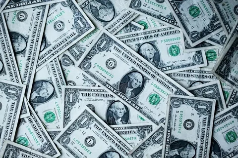Pile of US one dollar bills scattered and overlapping with George Washington's portrait visible on each note