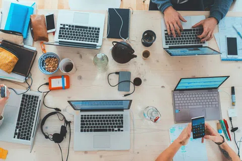 Overhead view of a collaborative workspace with laptops, notebooks, coffee, and people working together.